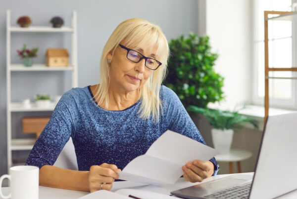 Woman at a home desk reading a printed rejection letter beside her open laptop