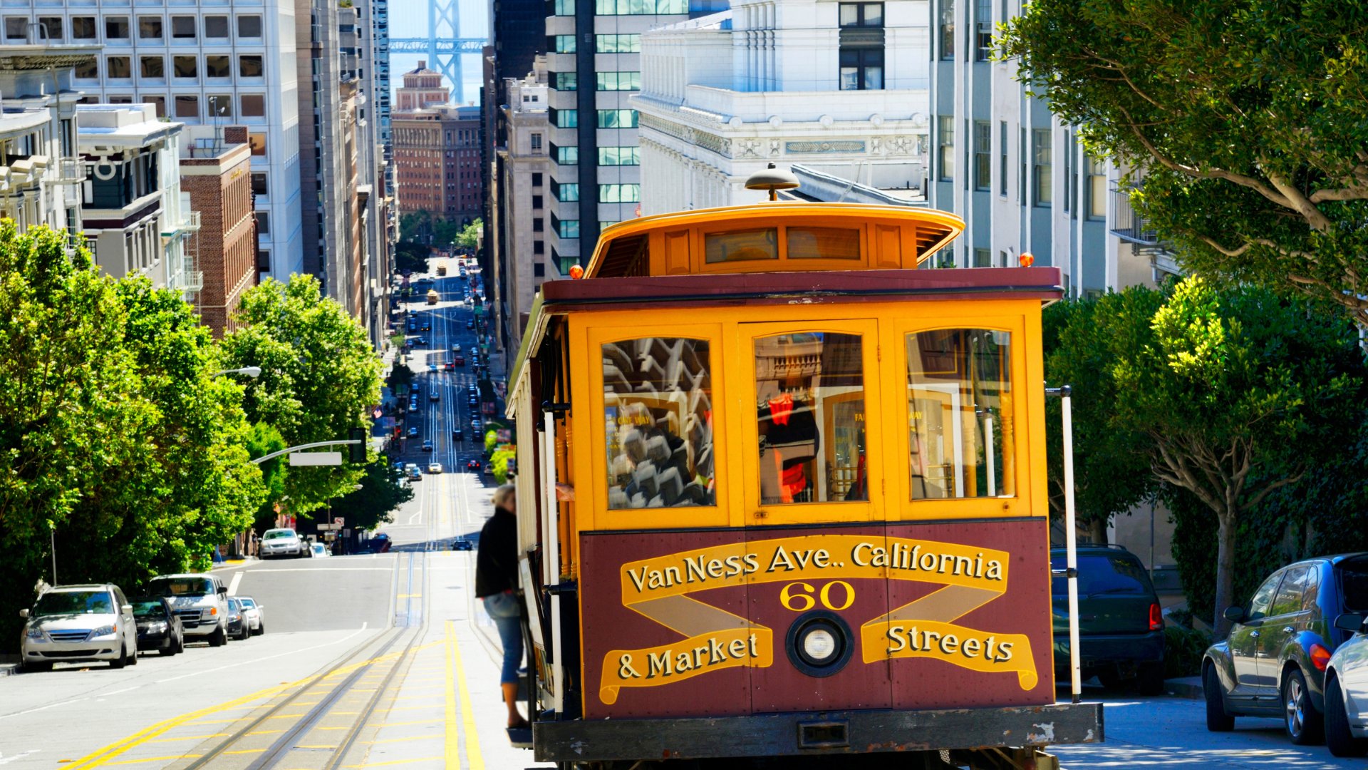 A San Francisco cable car climbing a steep hill with the Bay Bridge visible in the background.