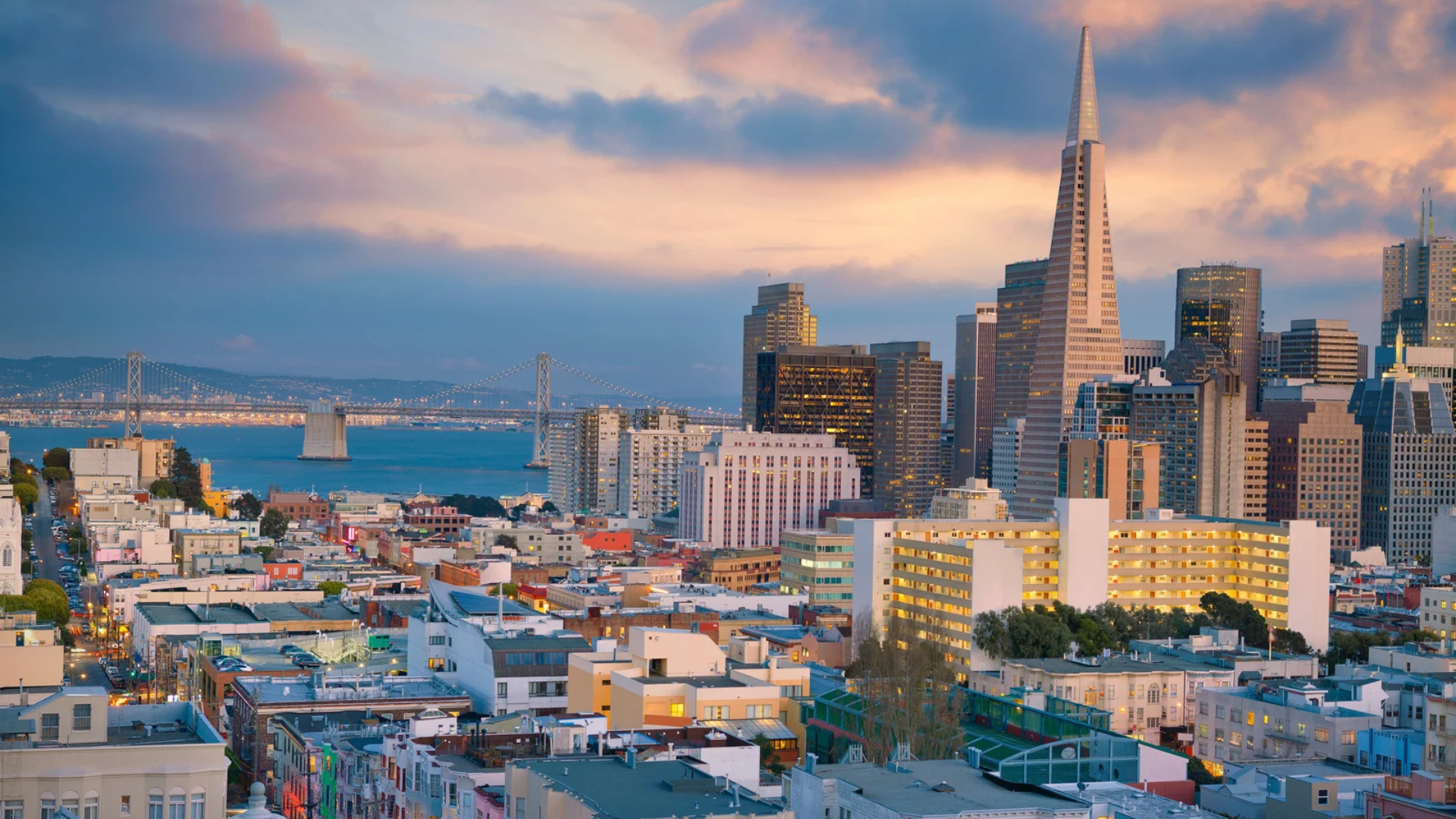 The San Francisco skyline at dusk, including the Transamerica Pyramid and the Bay Bridge in the distance.