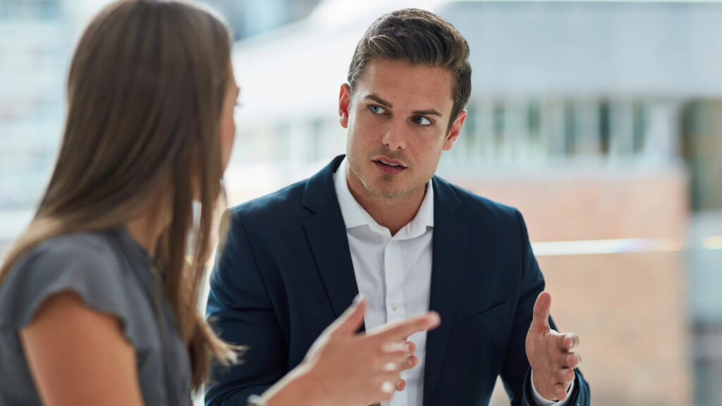 Two colleagues talking in a bright office, one gesturing as he explains a point to the other