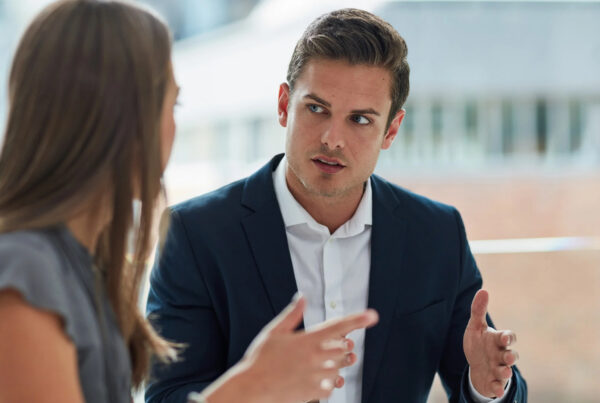 Two colleagues talking in a bright office, one gesturing as he explains a point to the other