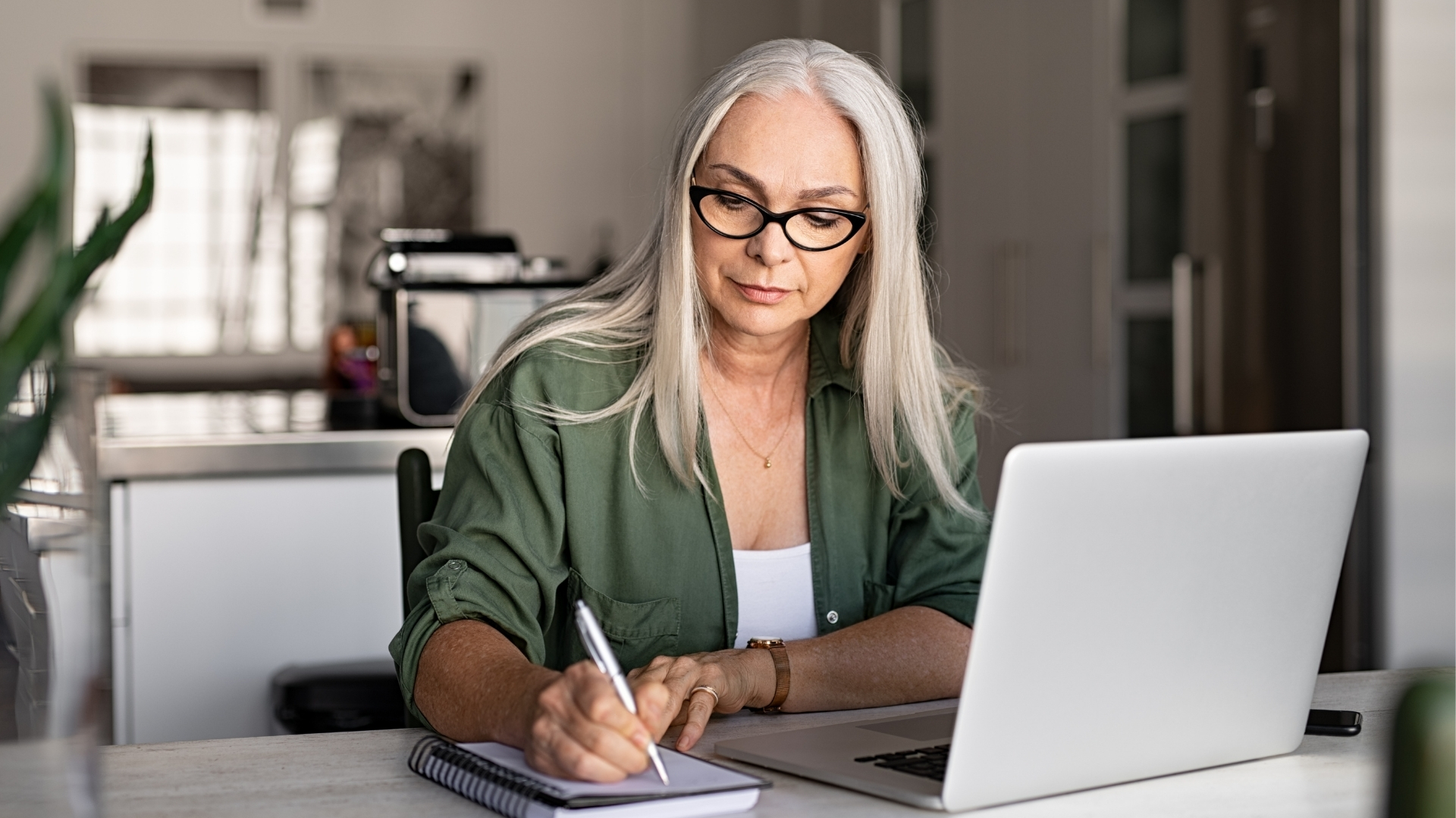 An employee writes notes in a notebook beside a laptop, documenting details after an AI layoff.