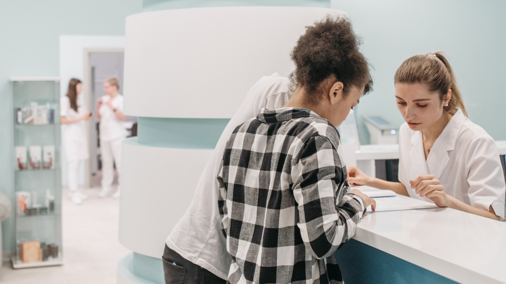Medical assistant helps a patient with forms at a clinic front desk, a workplace an Encino employment lawyer knows well