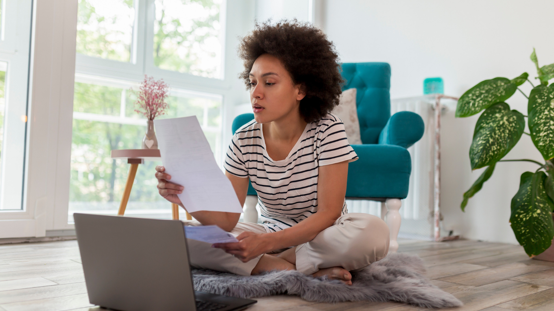 Employee sitting on her living room floor reviewing a pay stub beside a laptop to check for missed rest break pay