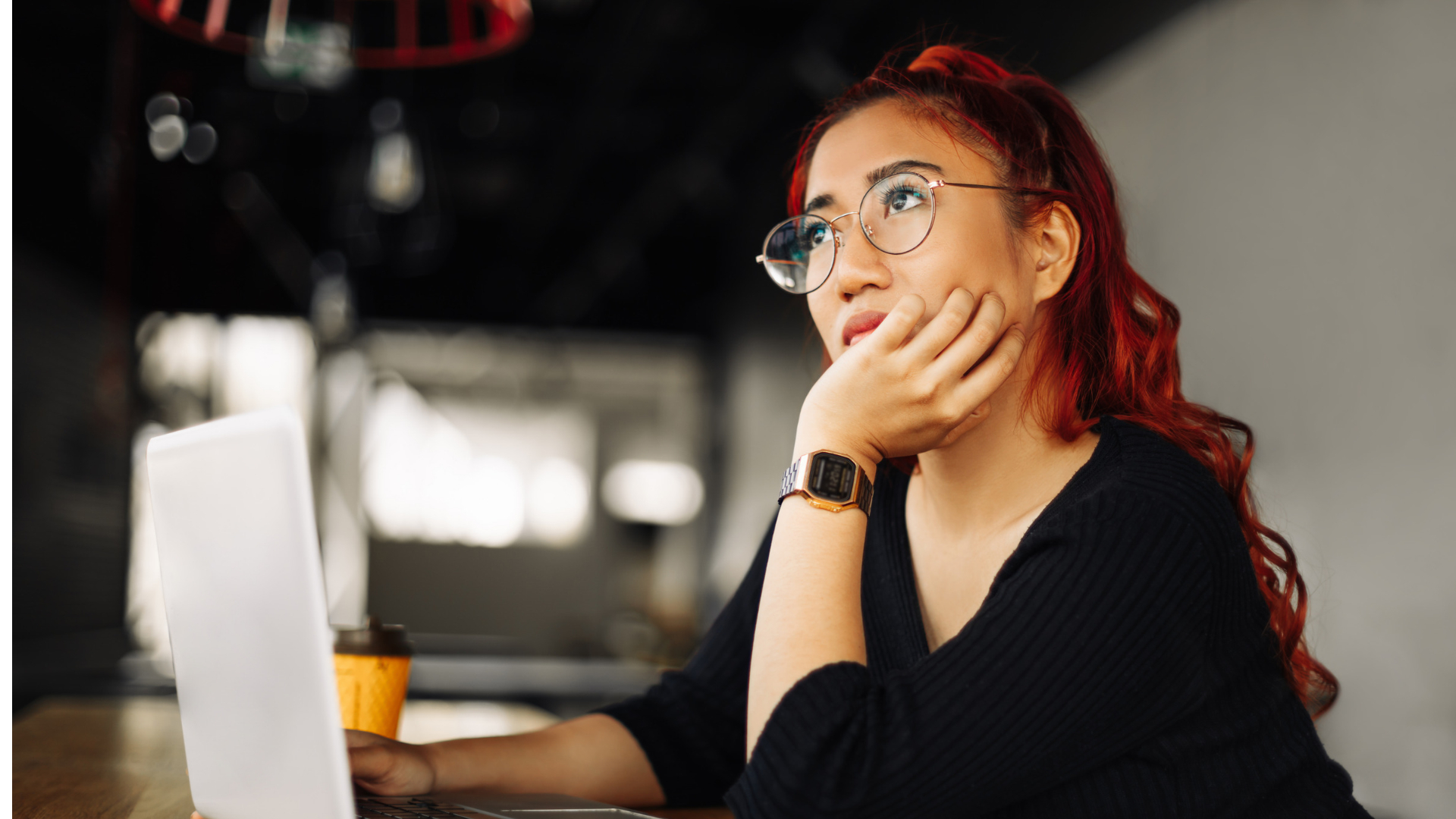 Employee in glasses pauses at her laptop in a cafe, thinking about whether to talk to a sexual harassment attorney