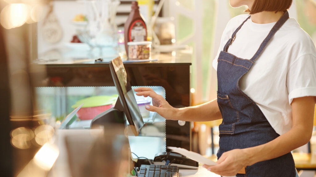 Restaurant employee in a denim apron tapping a POS touchscreen, a front-of-house role California restaurant break laws protect